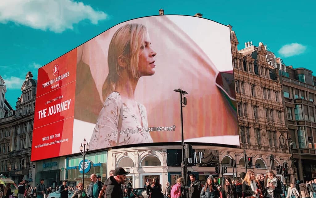 Large Turkish Airlines advertisement on a curved digital screen above a busy shopping street.