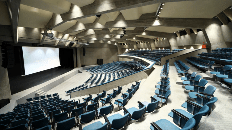 Large auditorium with tiered blue seating and stage.